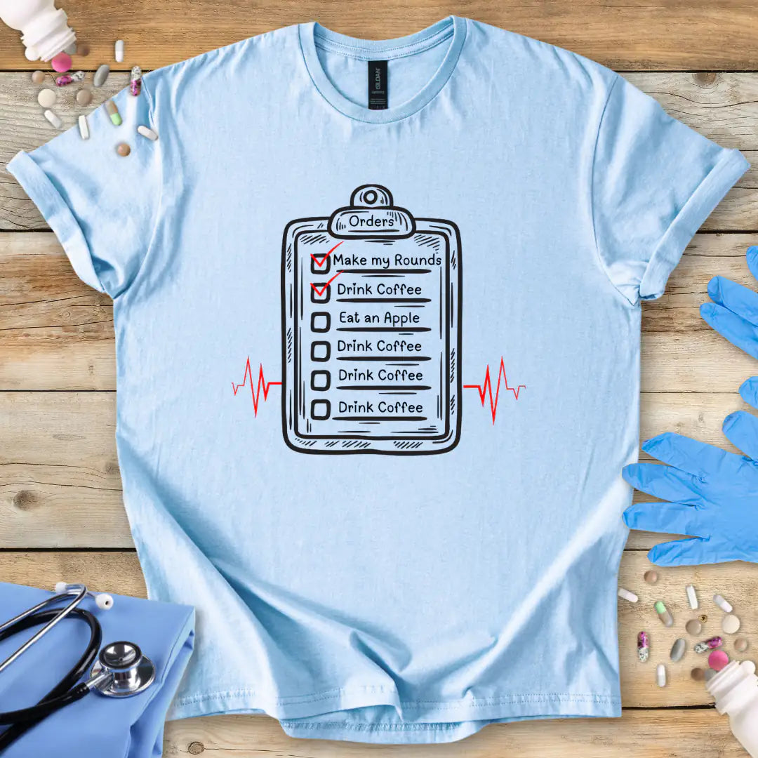 Light blue t-shirt with a medical-themed graphic on a wooden surface with medical accessories.