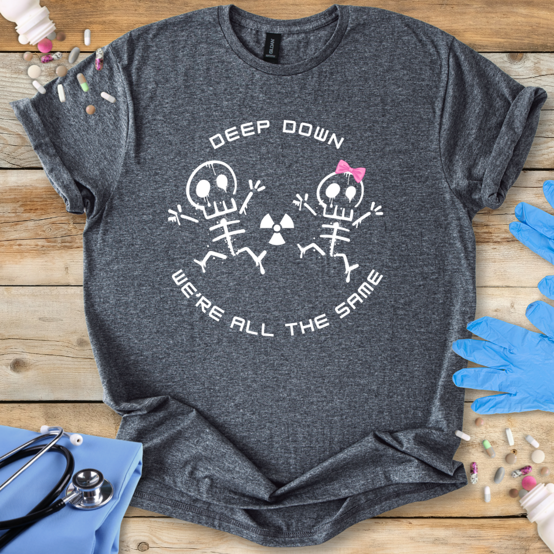 Grey med t-shirt with radiology skeleton design and 'Deep down we are all the same' text on a wooden surface with medical supplies.