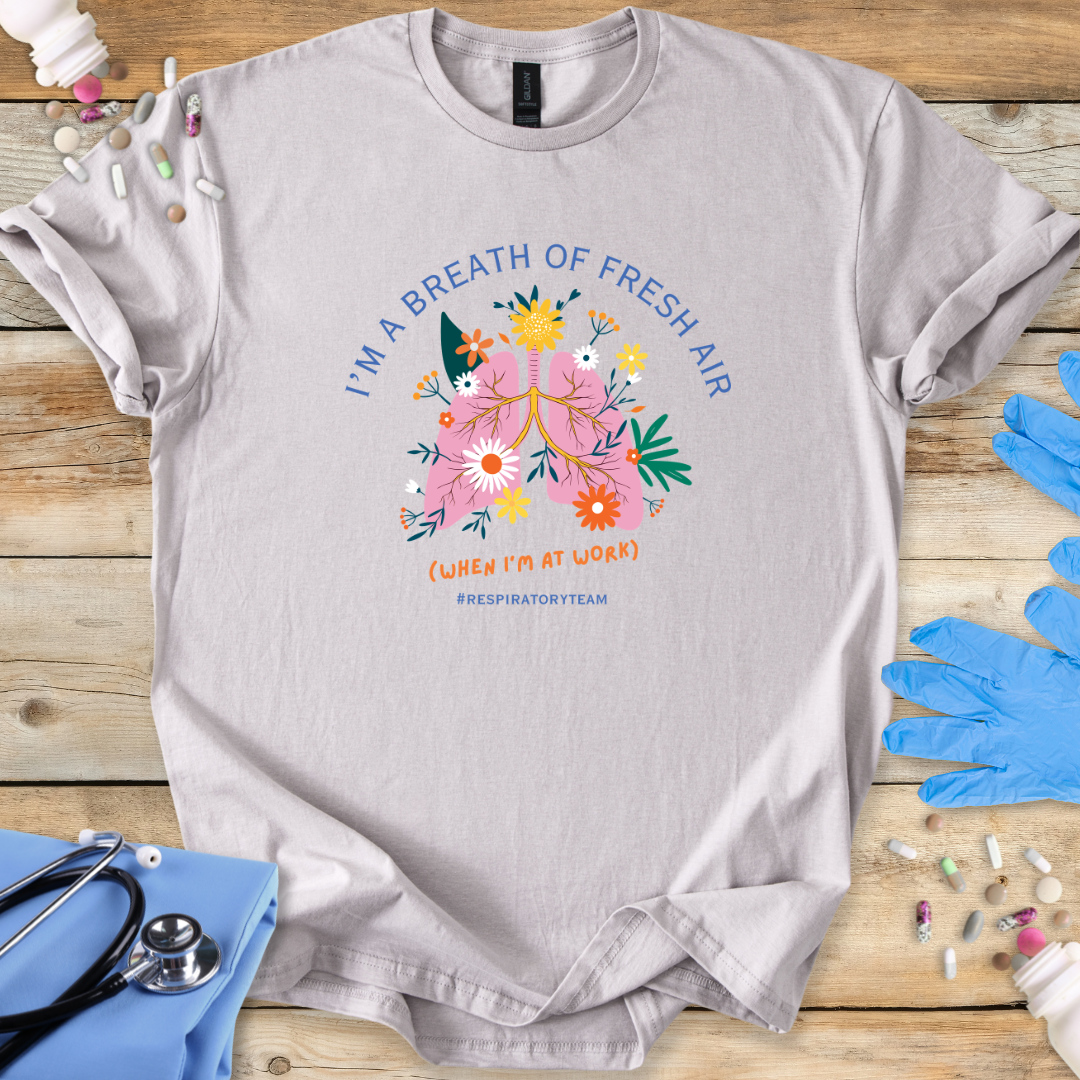 Ice-Gray med t-shirt with a colorful respiratory therapy graphic and 'I'm a breath of fresh air' text on a wooden surface with medical supplies.