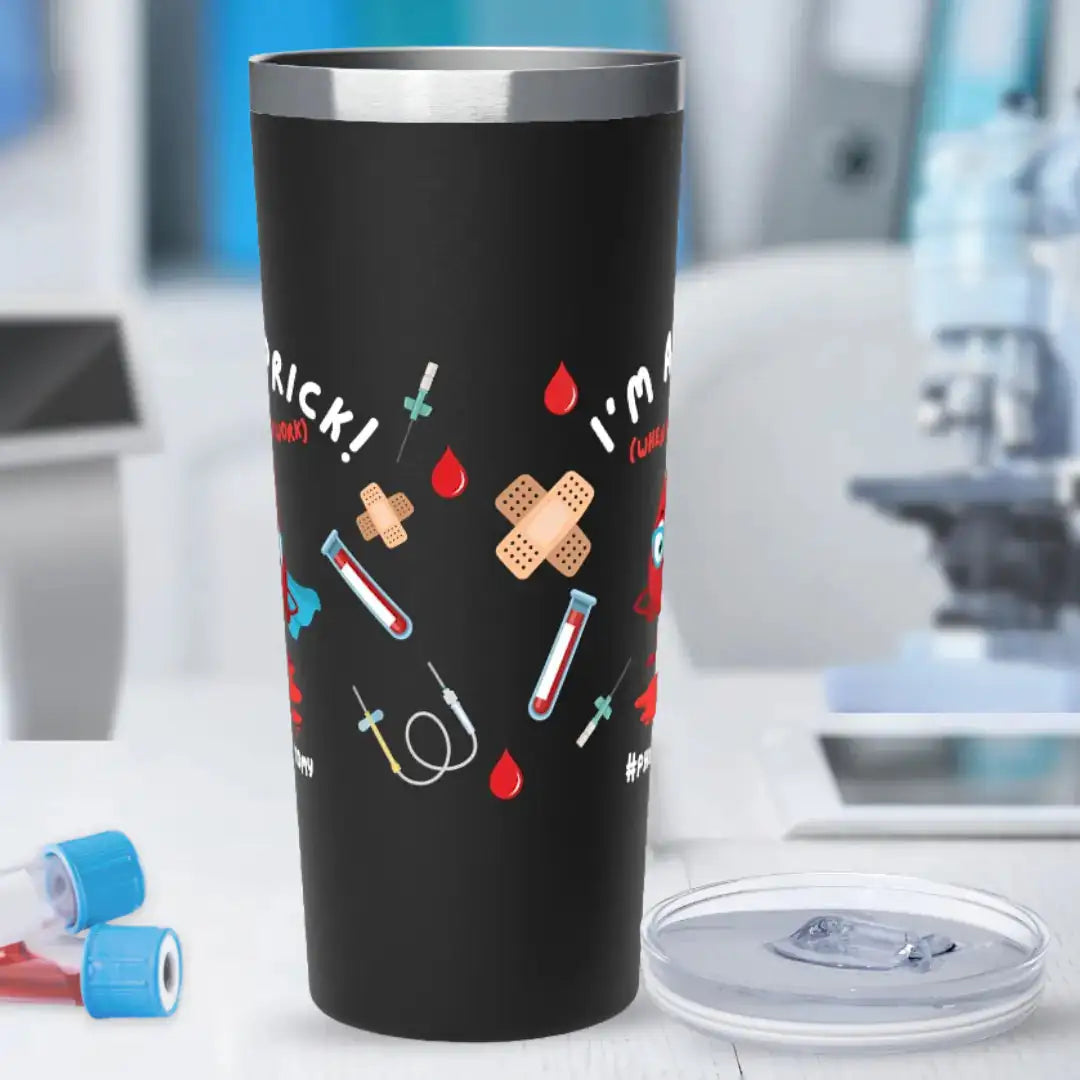 Black stainless steel tumbler with 'I'm A Prick! (When I'm At Work) #Phlebotomy' text and scattered blood drop, bandage, syringe, and blood vial graphics, on a blurred laboratory background.