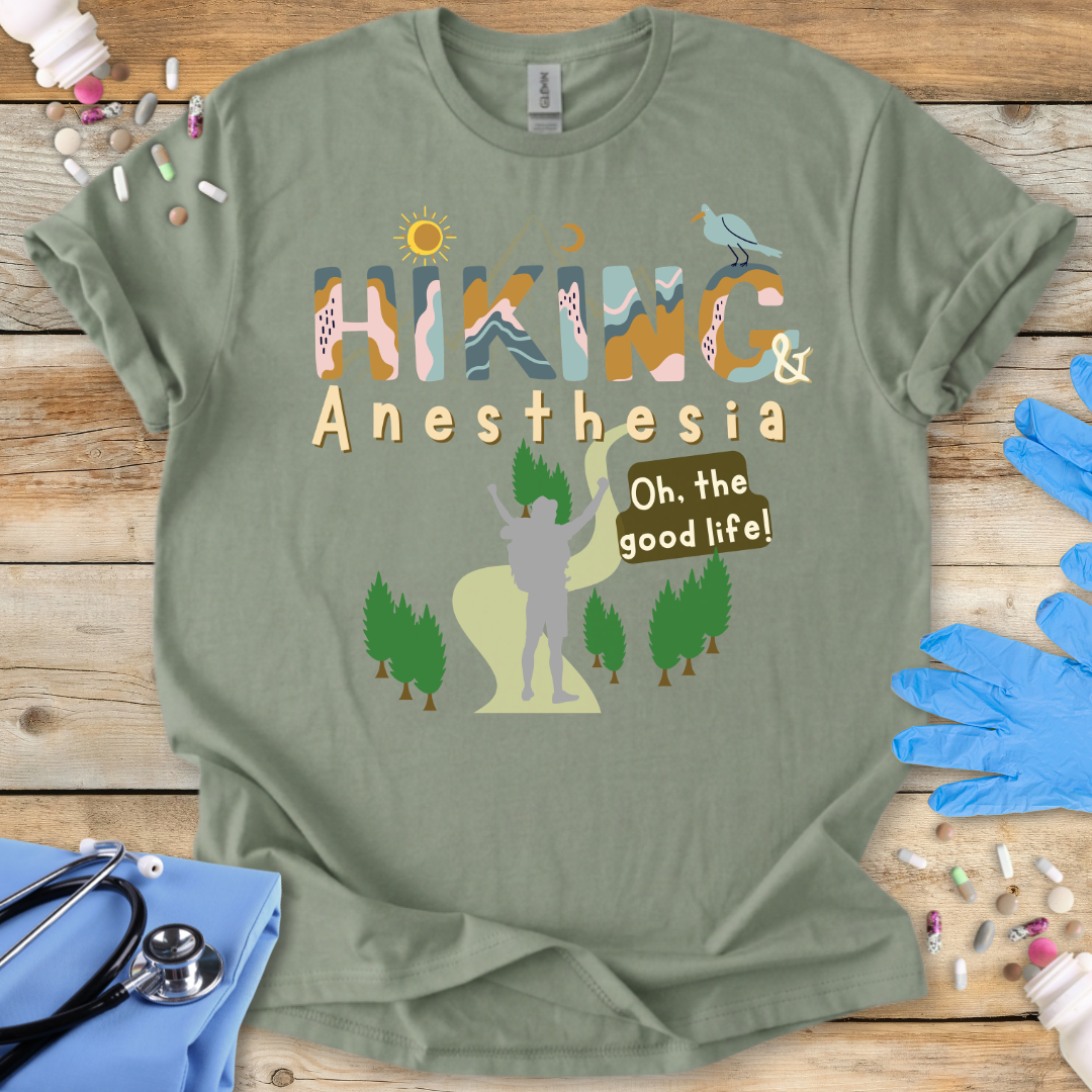 Green t-shirt with 'Hiking & Anesthesia Oh, the good life!' design on a wooden surface with medical supplies.