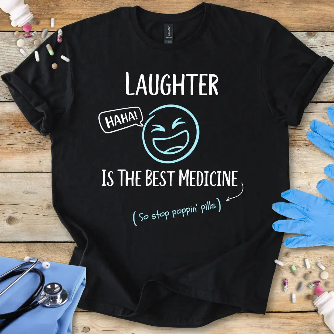 Black t-shirt with 'Laughter is the best medicine' text on a wooden surface with medical items.