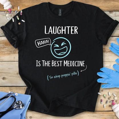 Black t-shirt with 'Laughter is the best medicine' text on a wooden surface with medical items.