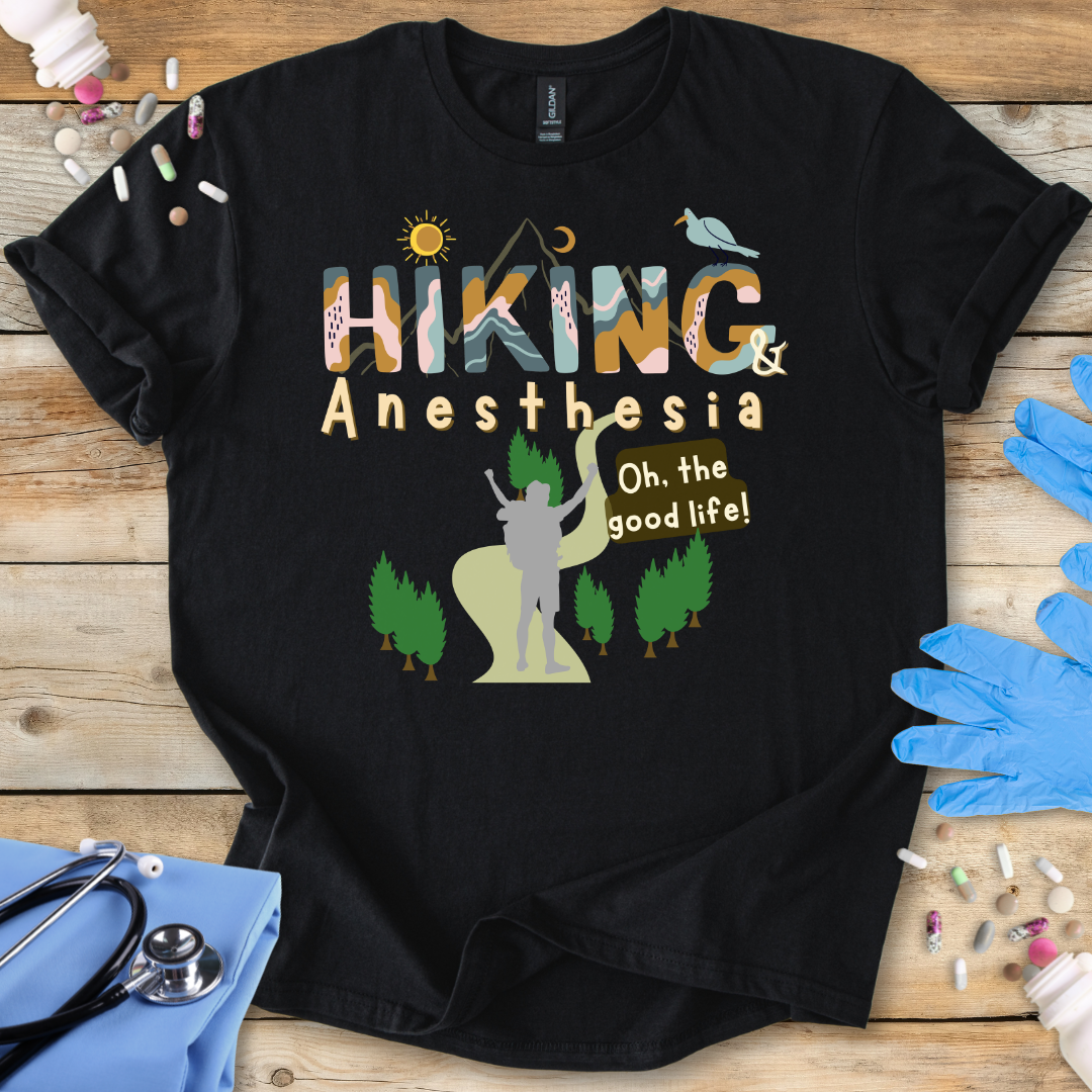 Black t-shirt with 'Hiking & Anesthesia Oh, the good life!' design on a wooden surface with medical supplies.