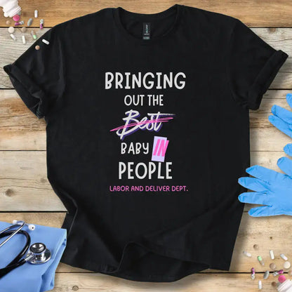 Black t-shirt with humorous 'Bringing out the baby in people' text design on a wooden surface with medical-themed Products