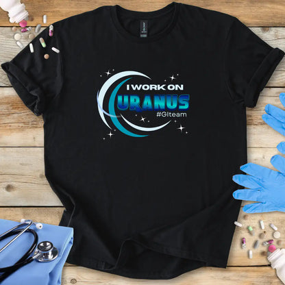 Black t-shirt with 'I Work on Uranus' graphic on a wooden surface with medical supplies.