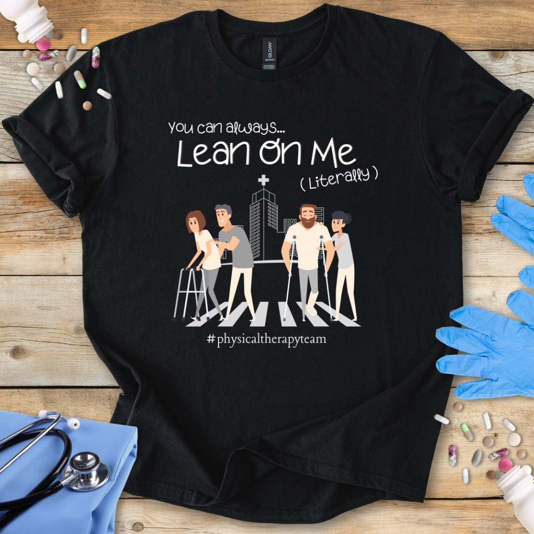 Black t-shirt with graphic design and 'Lean On Me' Physical therapy team' text on a wooden surface with medical accessories.