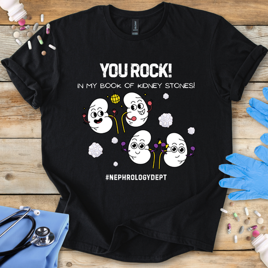 Black t-shirt with cartoon kidneys and 'You rock in my book of kidney stones, nephrology dept.' text on a wooden surface with medical accessories.