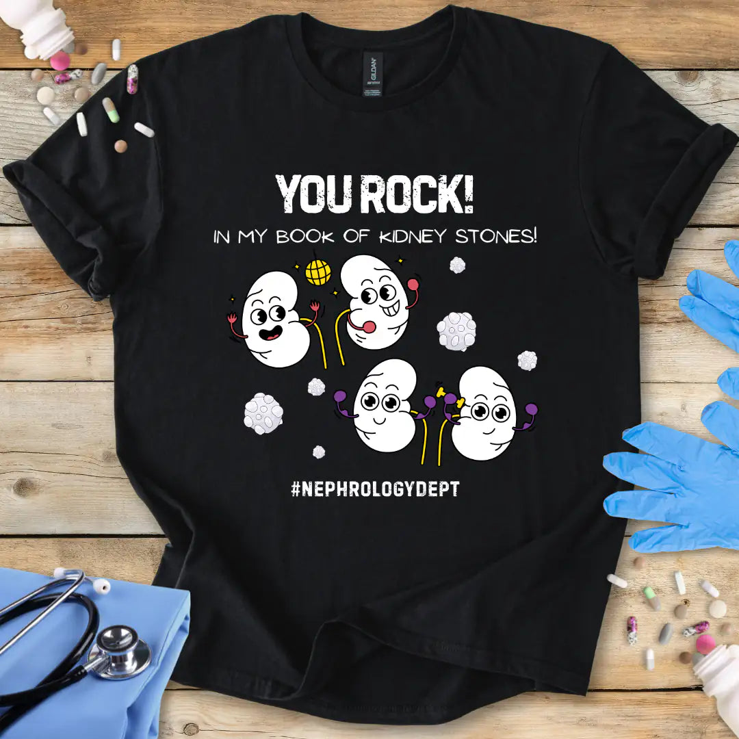 Black t-shirt with cartoon kidneys and 'You rock in my book of kidney stones, nephrology dept.' text on a wooden surface with medical accessories.