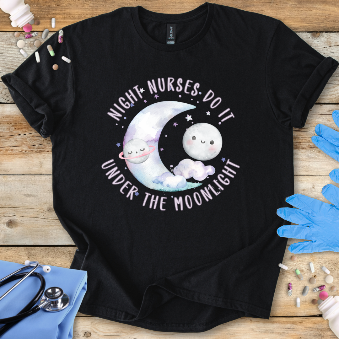 Black t-shirt with cartoon design and text 'Night nurses do it under the moonlight' on a wooden surface with medical supplies.