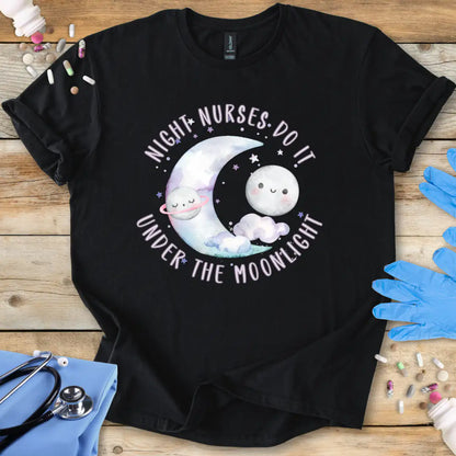 Black t-shirt with cartoon design and text 'Night nurses do it under the moonlight' on a wooden surface with medical supplies.