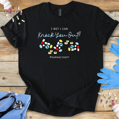 Black t-shirt with pharmacy-themed design with the text 'I bet i can knock you out' on a wooden surface with medical accessories.