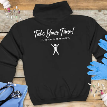 Black hoodie back printed with 'Take Your Time! Physical Therapy Dept.' in script and spaced lettering, featuring a white stick figure with arms raised, on a wooden background with stethoscope and medical gloves.
