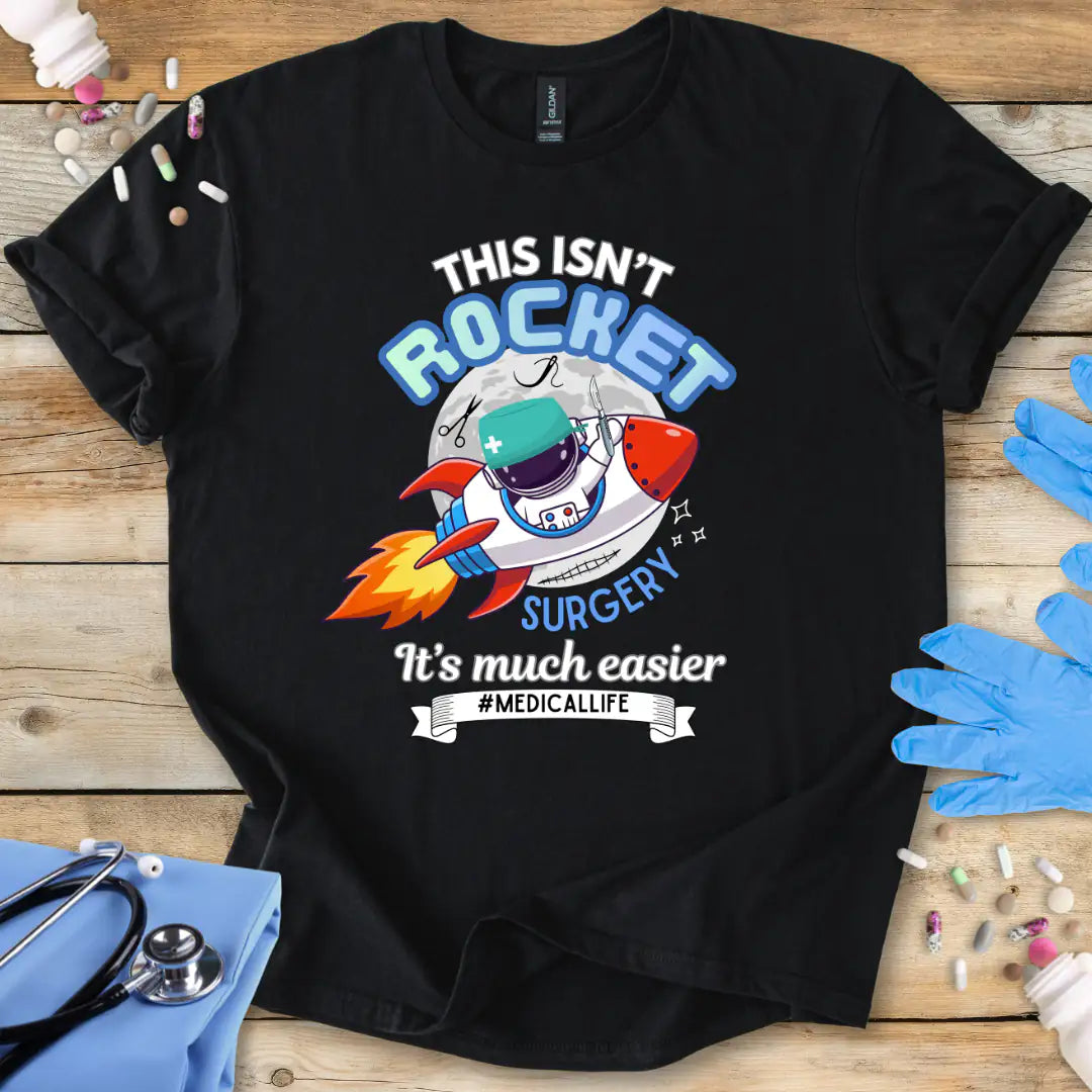 Black t-shirt with a humorous medical-themed graphic and 'This isn't rocket surgery' text on a wooden surface with medical accessories.