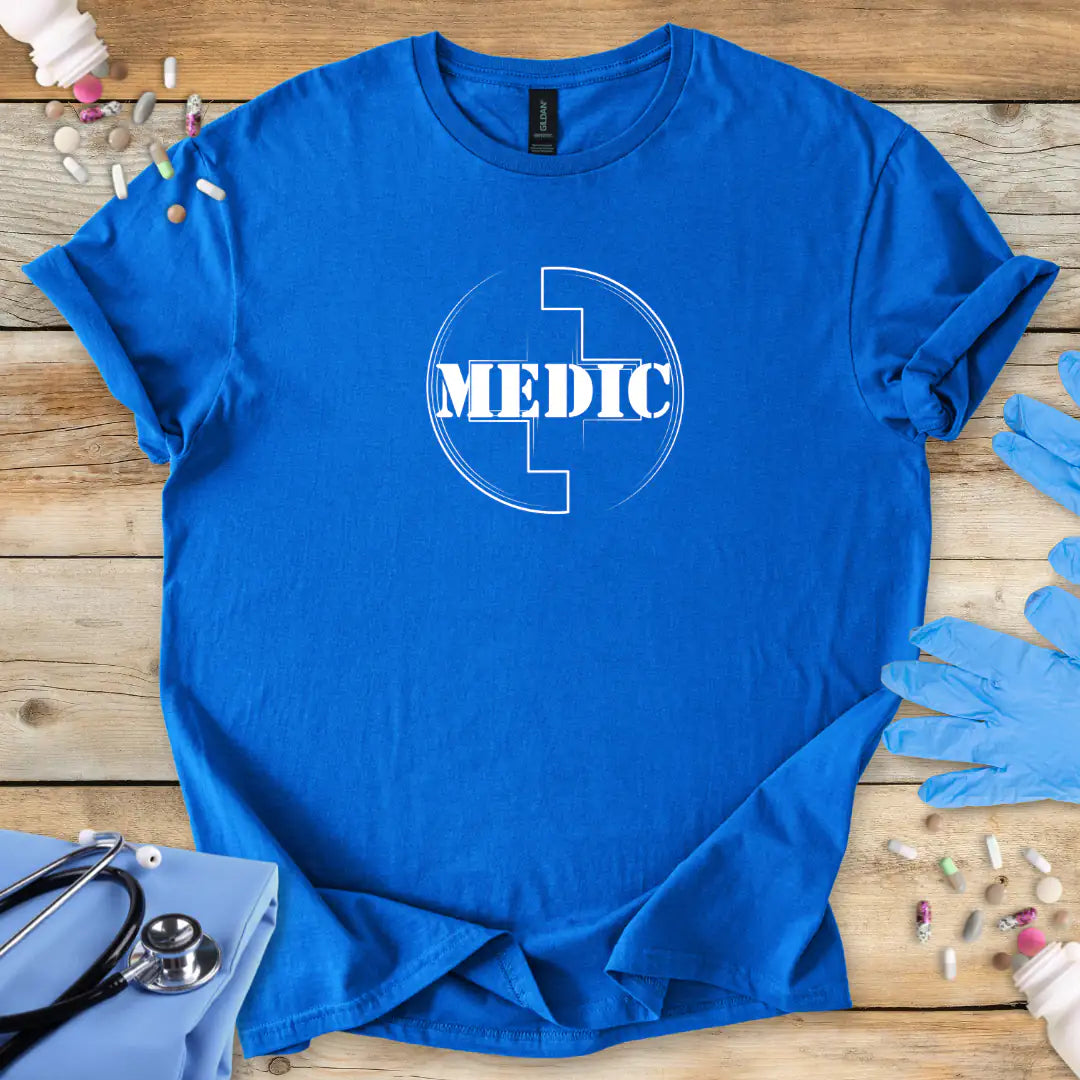 Blue t-shirt with 'MEDIC' symbol on a wooden surface with medical-themed items.