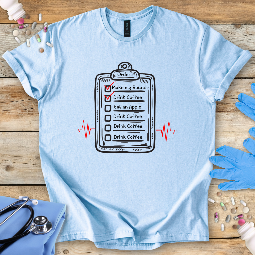 Light blue t-shirt with a medical-themed graphic on a wooden surface with medical accessories.