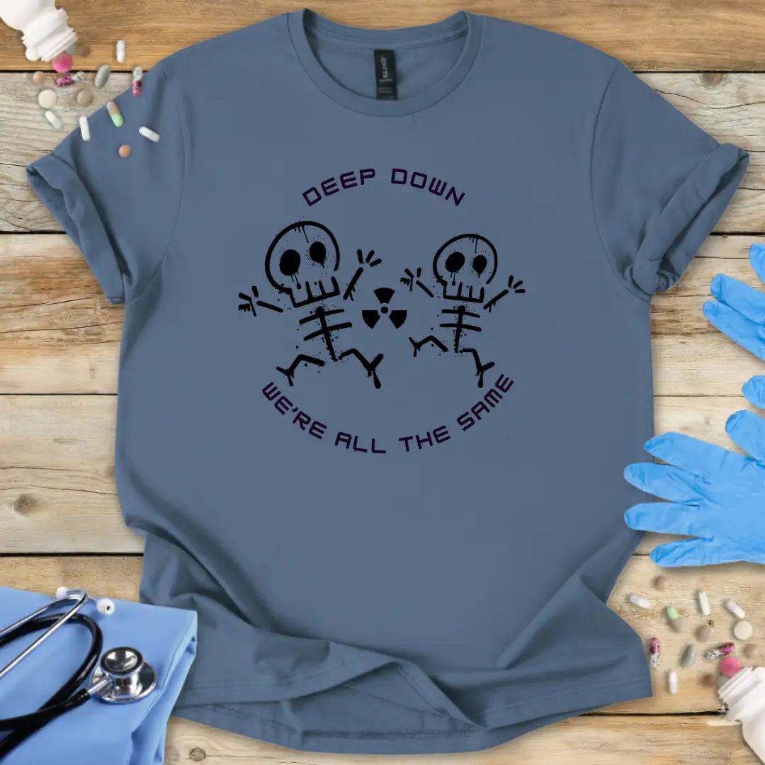 Blue t-shirt with skeleton design and text 'Deep Down We Are All The Same' on a wooden surface with medical supplies.