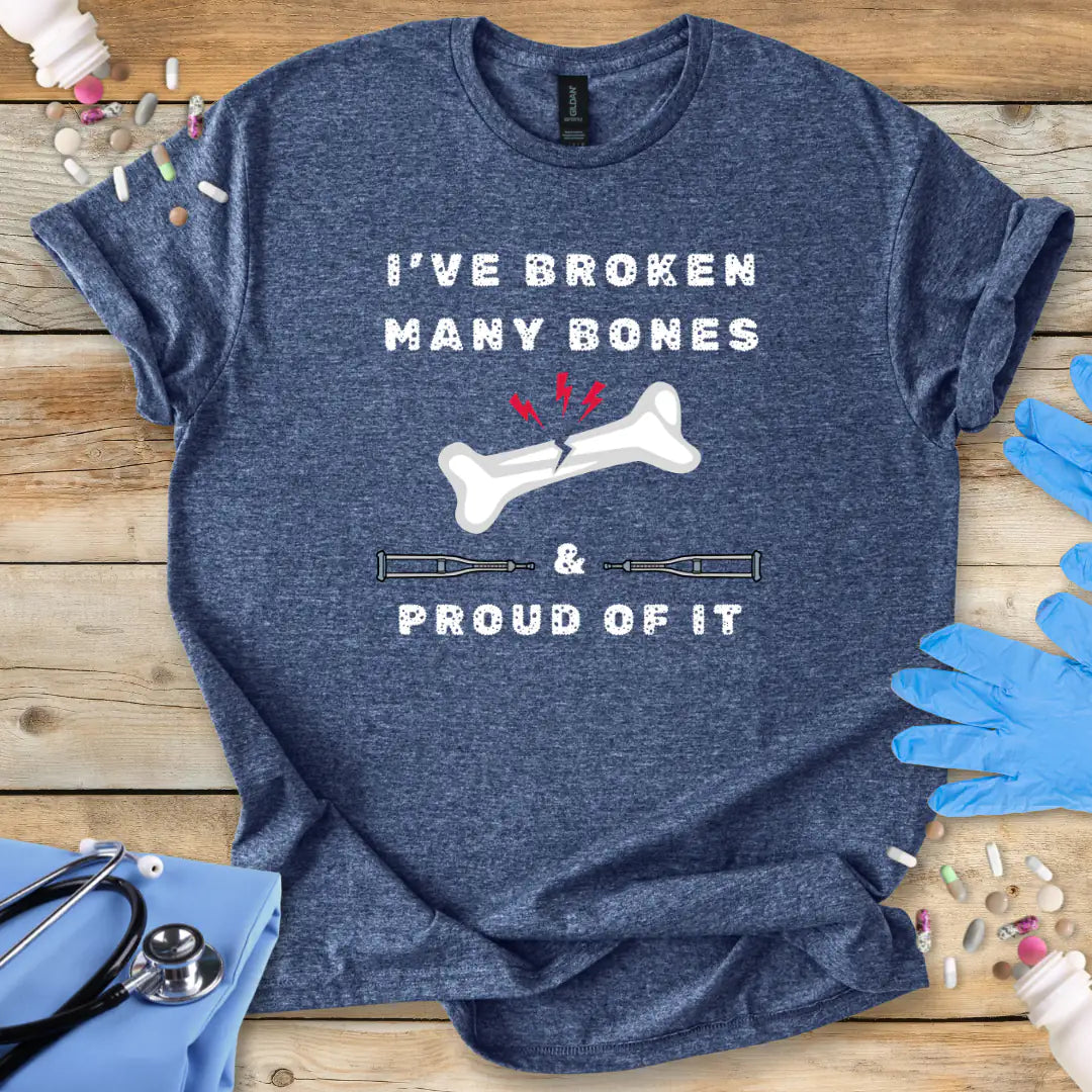 Blue med t-shirt with humorous text' I have broken many bones and proud of it' print on a wooden surface with medical accessories.