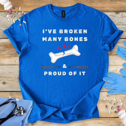 Royal Blue med t-shirt with humorous text' I have broken many bones and proud of it' print on a wooden surface with medical accessories.