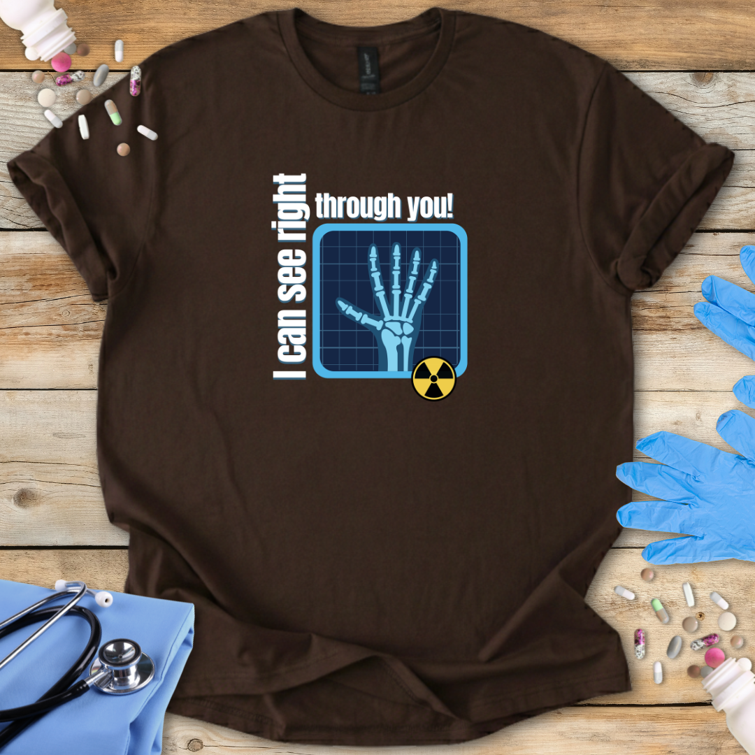 Brown med t-shirt with X-ray design and ' 'I can see right through you' text on a wooden surface with medical-themed items.