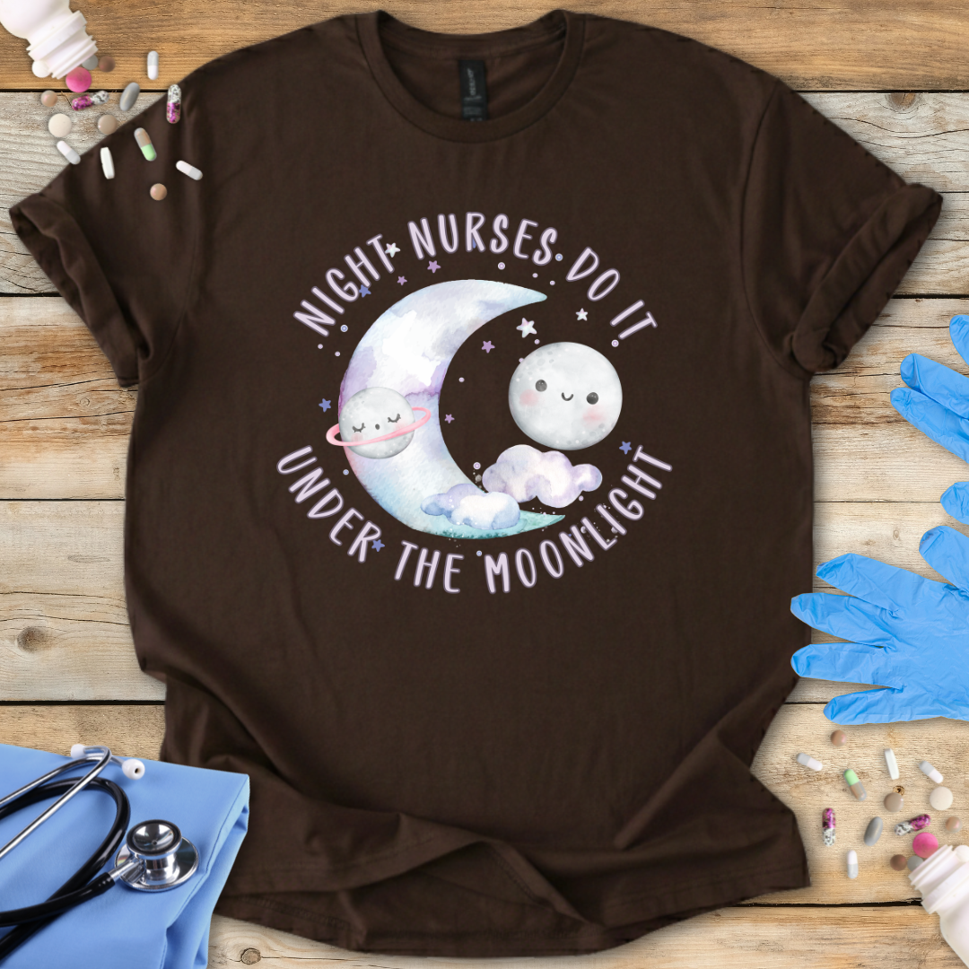 Brown t-shirt with cartoon design and 'Night-Nurses-Do-It-Under-The-Moonlight' text on a wooden surface with medical items.