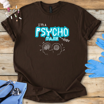 Brown t-shirt with 'I'm a Psycho Major' design on a wooden surface with medical supplies.