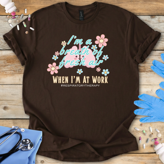 Brown t-shirt with lung cartoon character and 'I'm a breath of fresh air when I'm at work' text on a wooden surface with medical supplies.