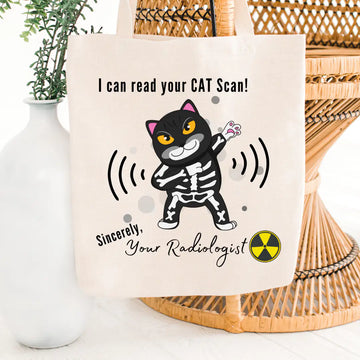 Tote bag with a cartoon cat skeleton and humorous text about reading CAT scans, placed on a woven surface.