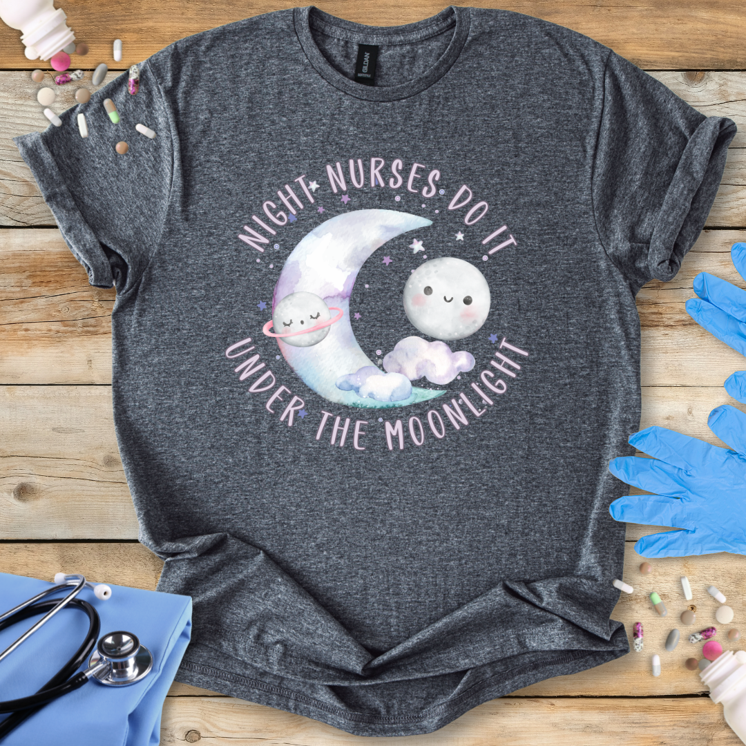 Dark Gray t-shirt with a moon and cloud design and text 'Night nurses do it under the moonlight' on a wooden surface with medical supplies.