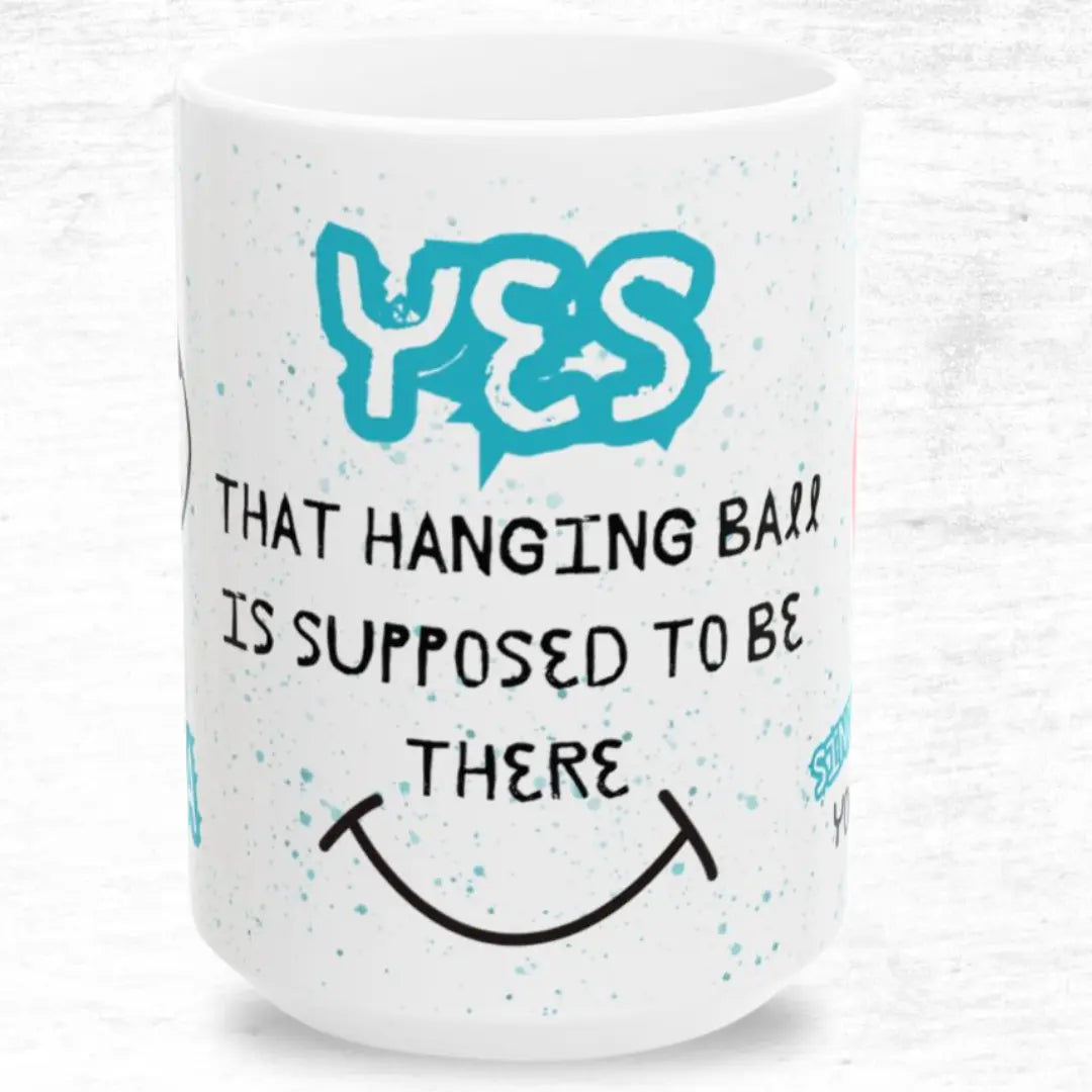 White mug with blue and black 'Yes that hanging ball is supposed to be there' text on a white background