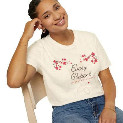 Woman wearing a natural color t-shirt with floral design and 'Every Patient Is My Patient' text, sitting on a chair.