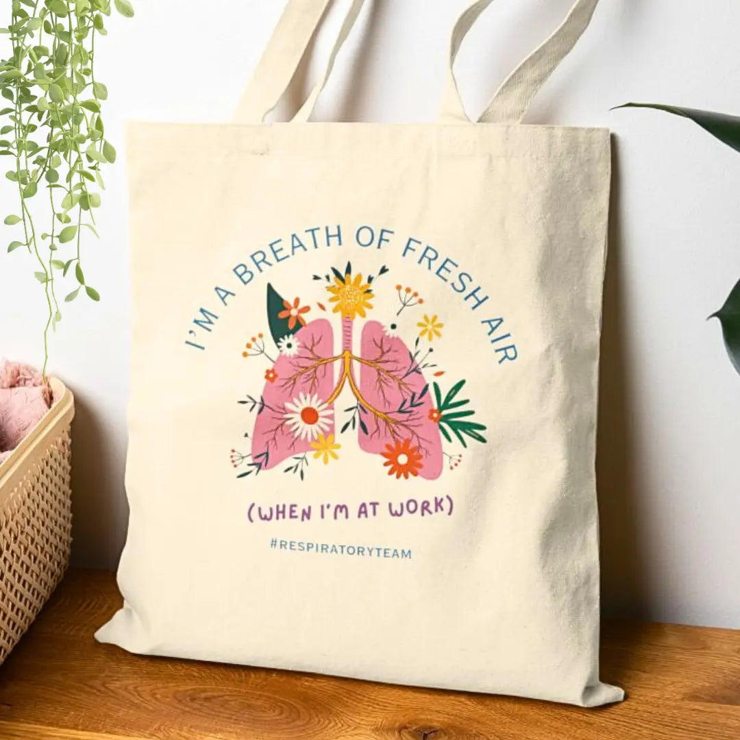 Tote bag with floral lungs design and 'I'm A Breath Of Fresh Air When I'm At Work' text on a wooden surface.