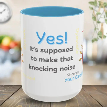 White mug with blue interior, text 'Yes! It's supposed to make that knocking noise. Sincerely, Your Cardiology team.