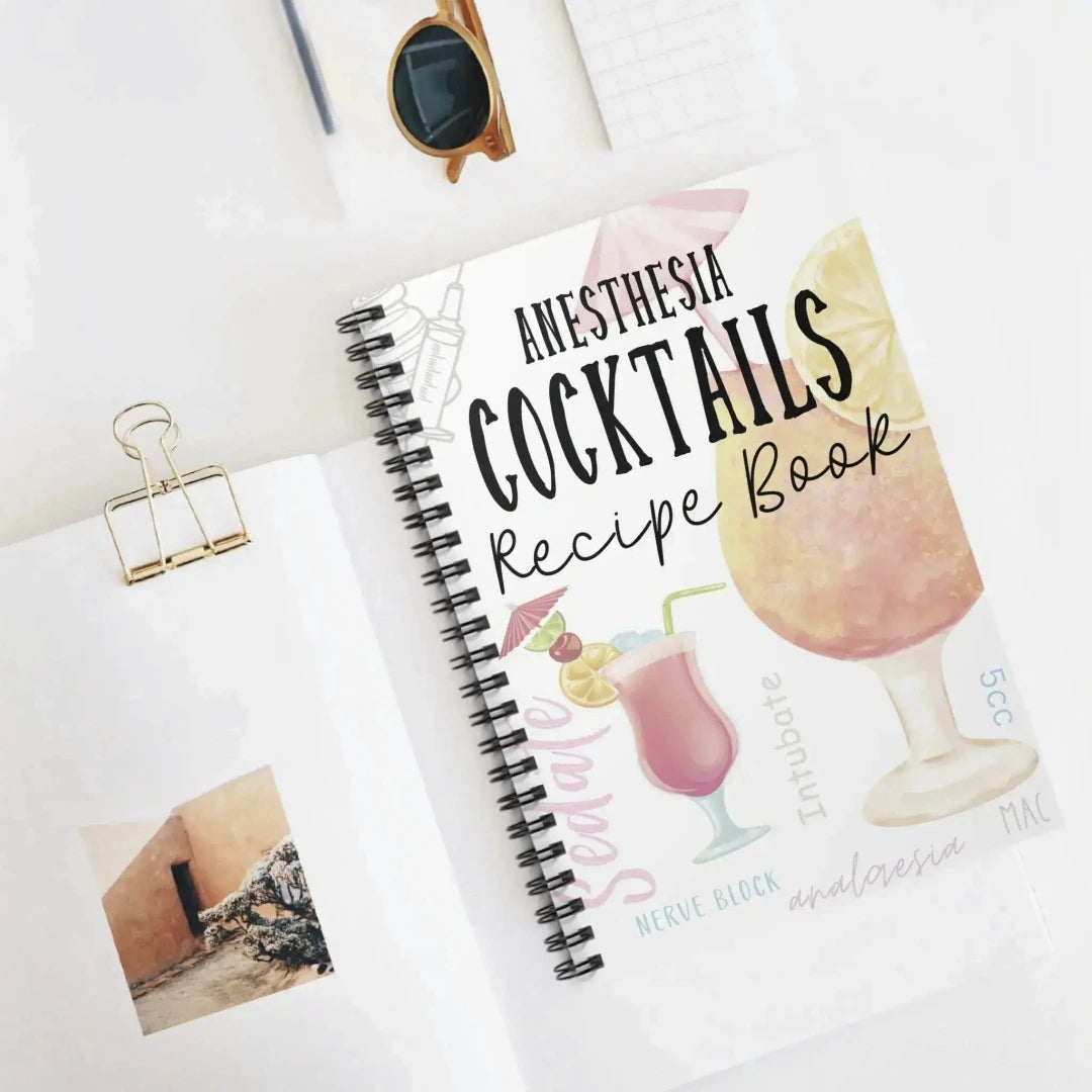Cookbook titled 'Anesthesia Cocktails Recipe Book' on a white surface with sunglasses and a photo clip.