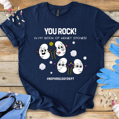 Navy t-shirt with cartoon kidneys and 'You rock in my book of kidney stones, nephrology dept.' text on a wooden surface with medical accessories.