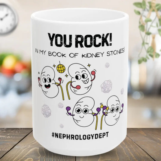 White mug with humorous cartoon kidneys and 'You Rock In My Book Of Kidney Stones' text on a wooden surface.
