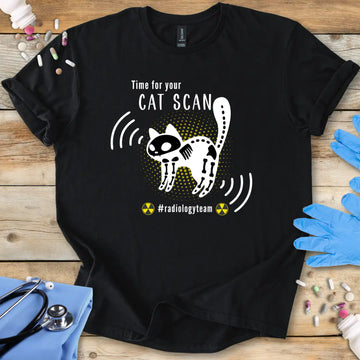 Black t-shirt with a cat scan radiology humor design and 'radiology team' text on a wooden surface with medical accessories.