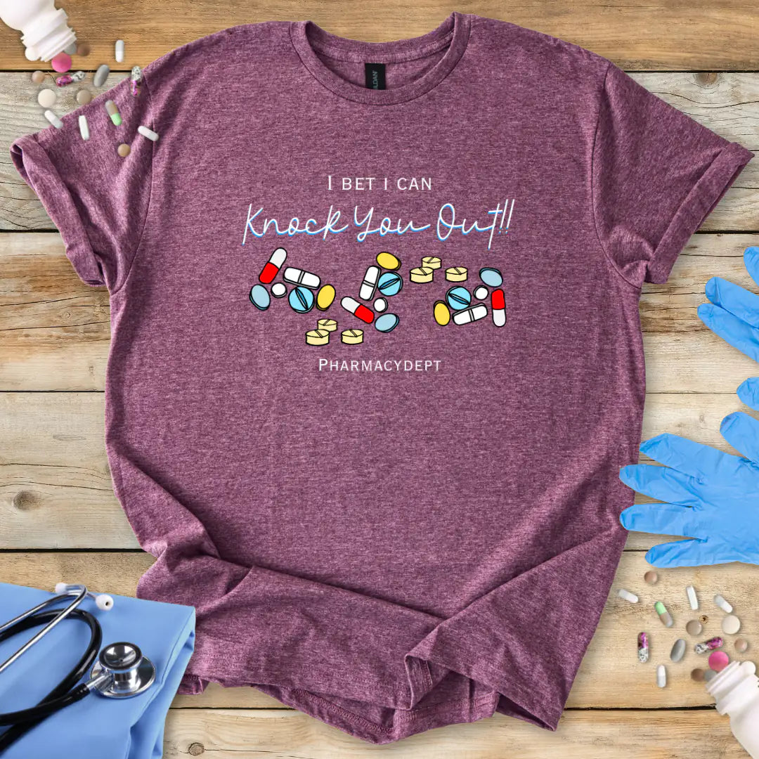 Gray t-shirt with pharmacy-themed design with the text 'I bet i can knock you out' on a wooden surface with medical accessories.