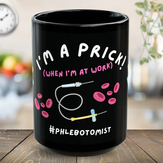 Black mug with humorous 'I'm a prick when I'm at work' text and graphics on a wooden surface
