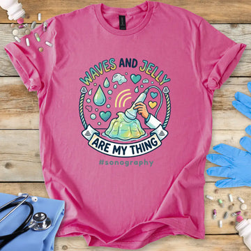 Pink t-shirt with sonography-themed design on a wooden surface with medical equipment.