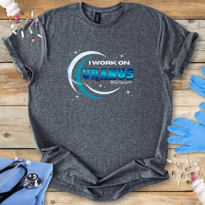 Gray t-shirt with 'I Work on Uranus' graphic on a wooden surface with medical supplies.