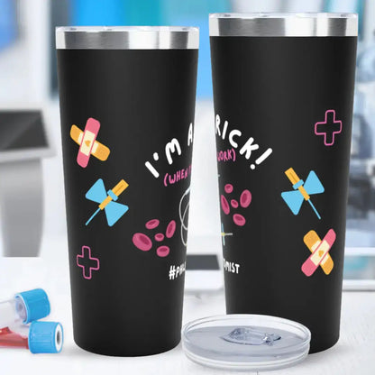 Two black stainless steel tumblers showing front and back views with 'I'm A Prick! (When I'm At Work) #Phlebotomist' text, decorated with colorful bandage, butterfly needle, red blood cell, and medical cross graphics, on a blurred laboratory background.
