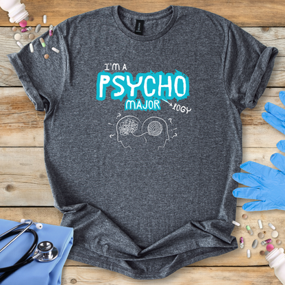 Gray t-shirt with 'I'm a Psycho Major' design on a wooden surface with medical accessories.