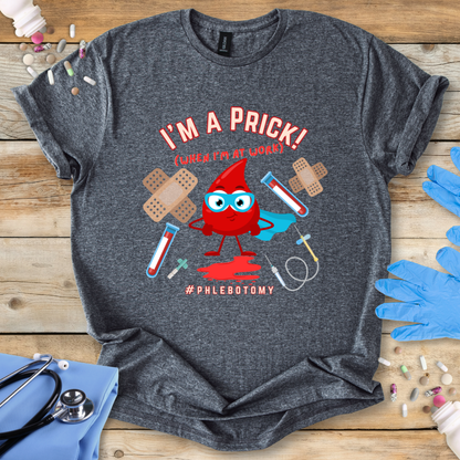 Dark Heather Gray t-shirt with a graphic design featuring a blood drop character and text 'I'm A Prick Phlebotomy' on a wooden surface with medical accessories.