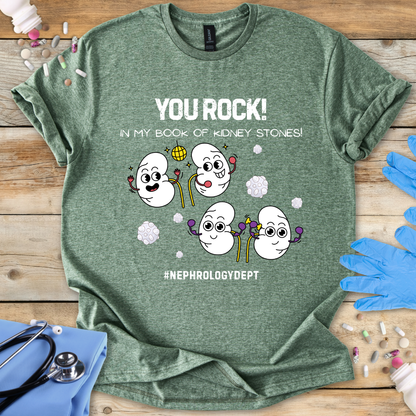 Military Green t-shirt with cartoon kidneys and 'You rock in my book of kidney stones, nephrology dept.' text on a wooden surface with medical accessories.