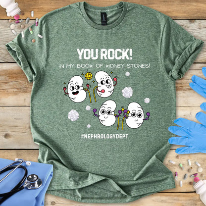 Military Green t-shirt with cartoon kidneys and 'You rock in my book of kidney stones, nephrology dept.' text on a wooden surface with medical accessories.
