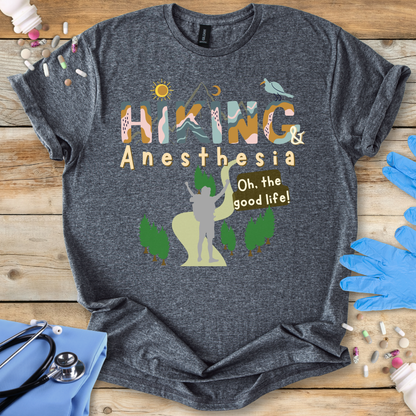 Gray t-shirt with 'Hiking & Anesthesia Oh, the good life!' design on a wooden surface with medical supplies.