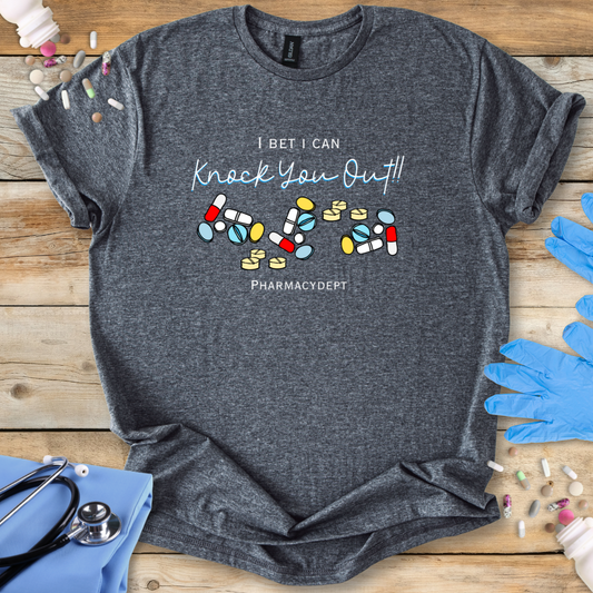 Gray t-shirt with pharmacy-themed design with the text 'I bet i can knock you out' on a wooden surface with medical accessories.