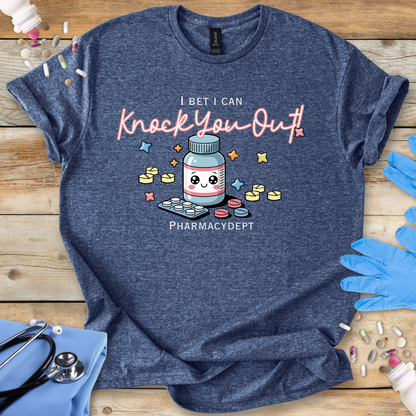 Heather Navy t-shirt with a pharmacy-themed graphic and 'I bet I can knock you out' text on a wooden surface with medical accessories.