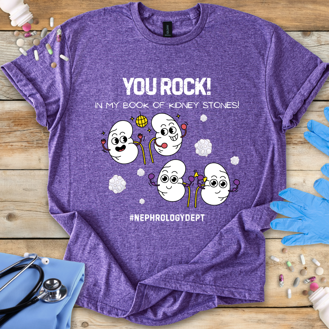 Heather purple t-shirt with cartoon kidneys and 'You rock in my book of kidney stones, nephrology dept.' text on a wooden surface with medical accessories.